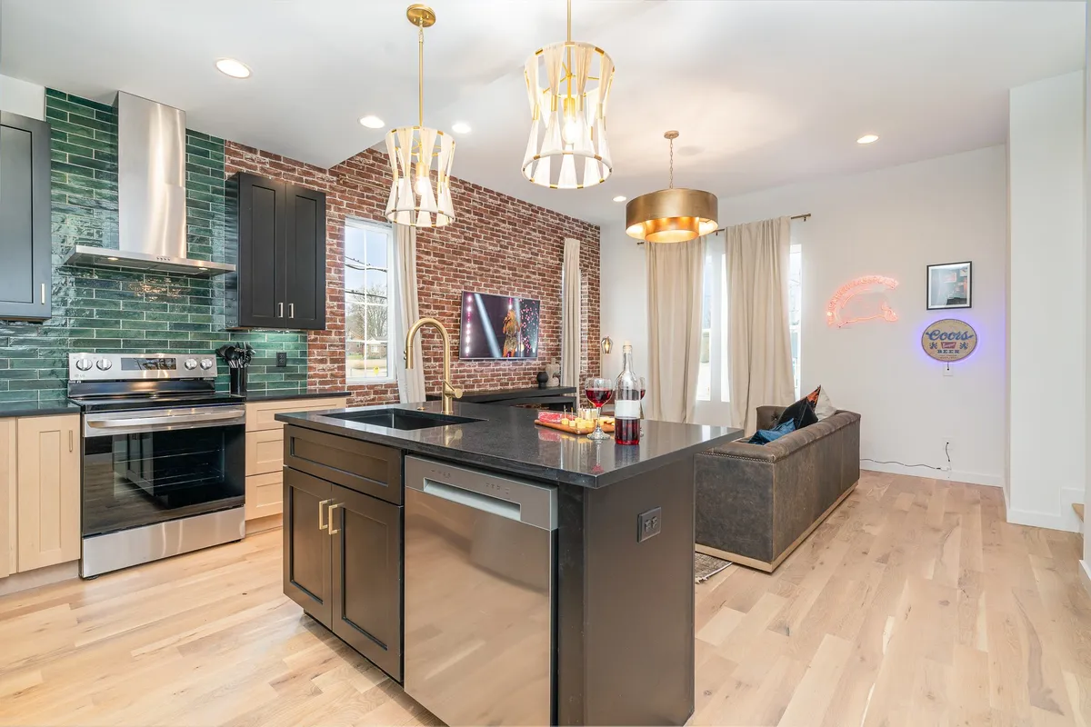 A lively interior featuring a kitchen island with pendant lights, exposed brick wall, and a sofa nearby. The layout emphasizes interaction between kitchen and living areas, suitable for both cooking and relaxing. The space radiates contemporary style and invites group activities.
