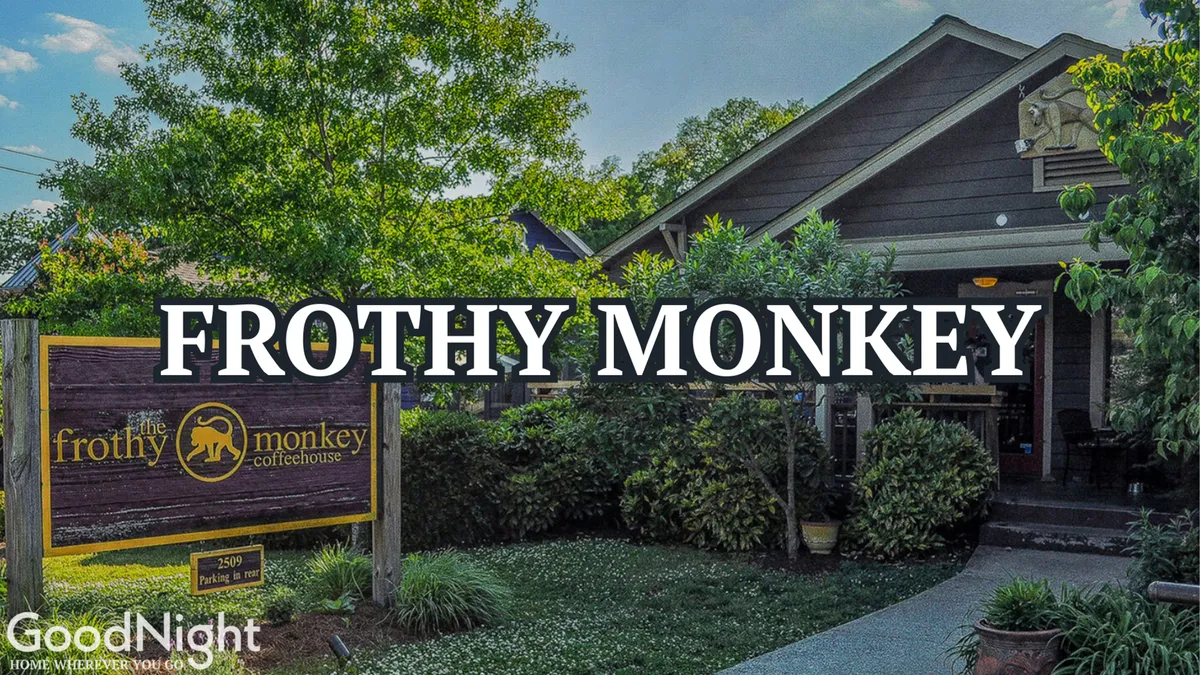 This image shows the exterior of Frothy Monkey, complete with clear signage and lush greenery surrounding the entrance. Outdoor seating creates an inviting and social atmosphere, and several people are visible enjoying coffee and conversation.