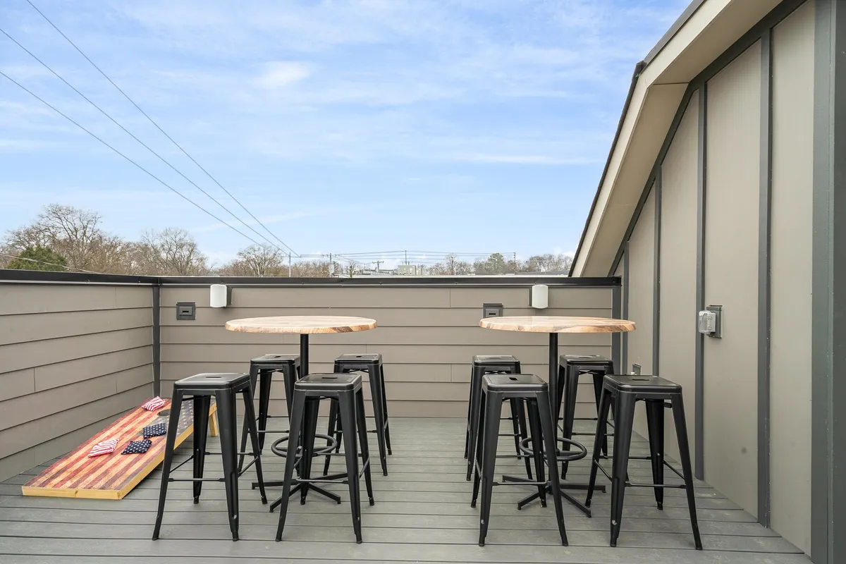 A modern rooftop setup with wooden tables and black stools offers panoramic outdoor views. The design is informal and functional, providing ample space for group games, casual dining, or simply soaking in the city atmosphere.