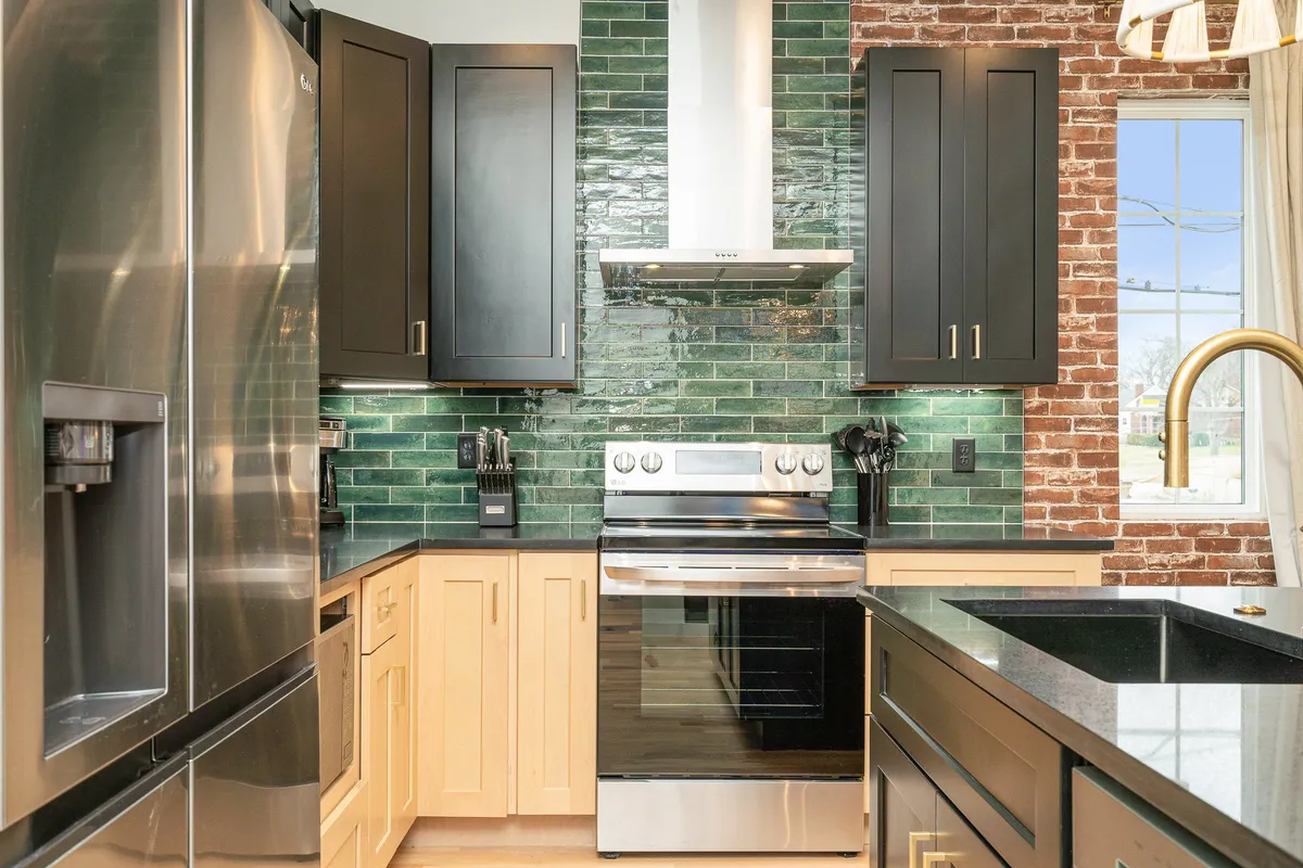 A contemporary kitchen featuring black cabinets, a vibrant green tile backsplash, and stainless steel appliances. The black countertops and open layout invite gatherings, with a setting ideal for cooking, entertaining, or family activities.