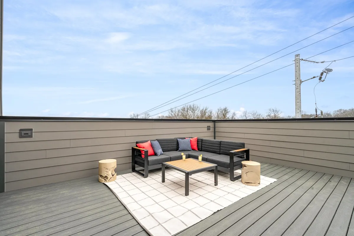 An inviting outdoor seating area featuring comfortable chairs with decorative cushions, a coffee table, and a stylish rug. The setting is perfect for group gatherings, morning coffee, or evening relaxation, and it connects seamlessly to the home’s exterior, suggesting an extension of the indoor living space into the outdoors.